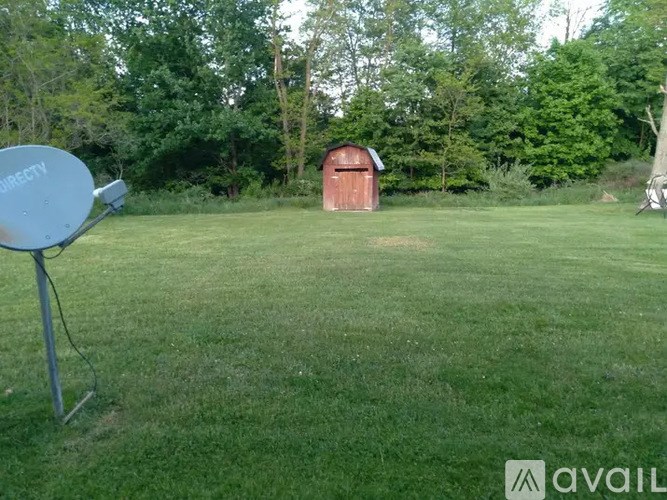 A satellite dish is on a lawn with a red shed in the background.