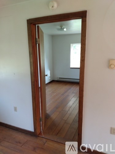 A large mirror on a white wall reflects a room with a wooden floor and a white ceiling.