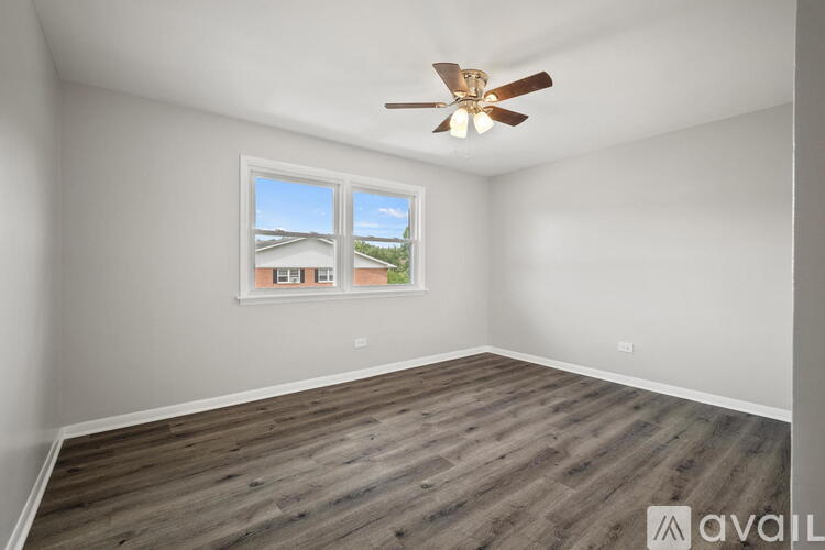 A room with a ceiling fan and a window showing a view of houses.