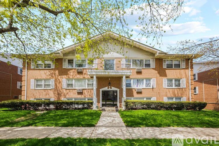 A brick apartment building with a front lawn and trees.