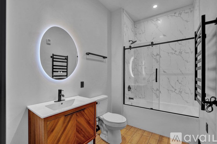 A bathroom with a marble shower and a round mirror.