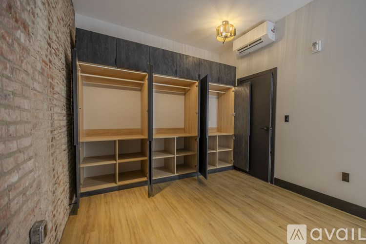 A room with a brick wall and wooden floors has a couple of shelving units and a door.