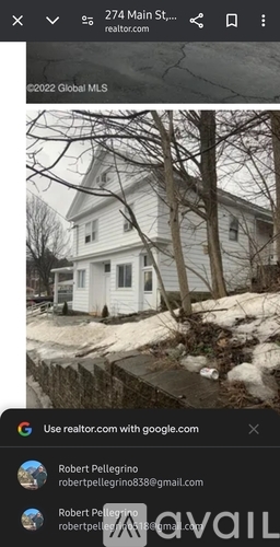 A white house with a snow-covered ground and bare trees in front.