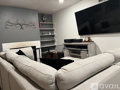 A living room with a white couch and a television mounted on the wall.