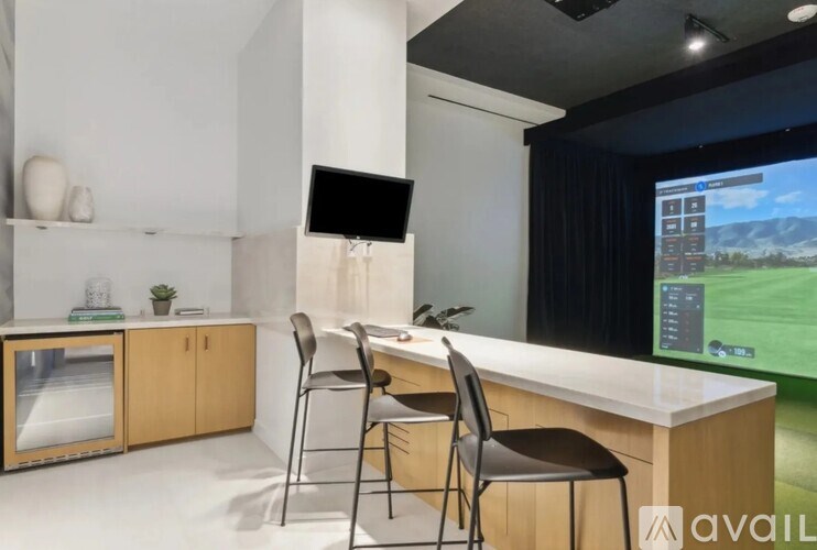 A modern office with a desk, chairs, and a large screen displaying a game.