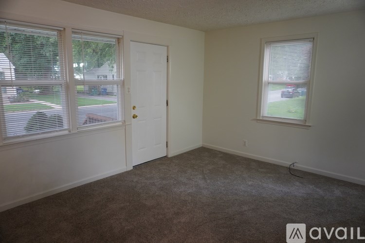 A room with a carpeted floor, a door, and a window with blinds.