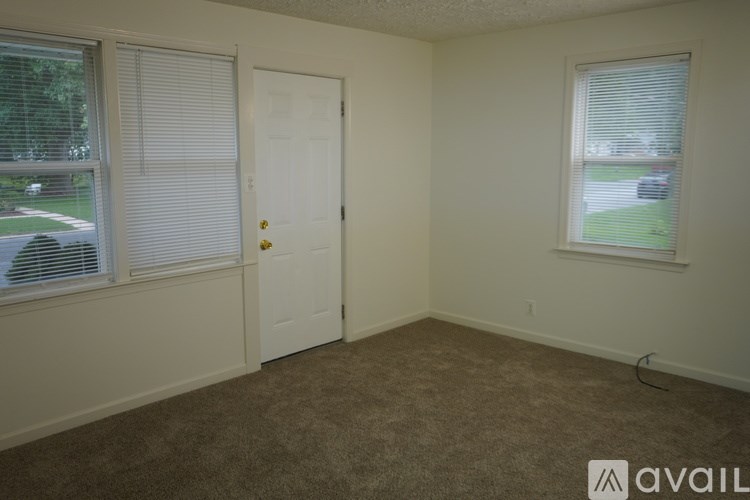 A room with a carpeted floor, a door, and a window with blinds.