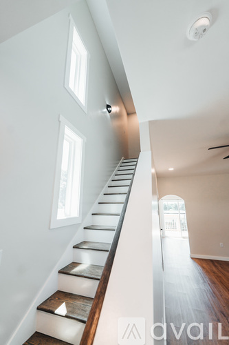 A staircase with a light brown wooden handrail and white steps leads up to a window.