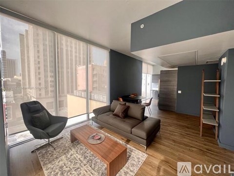 A living room with a brown couch, a black chair, and a coffee table in front of a large window.