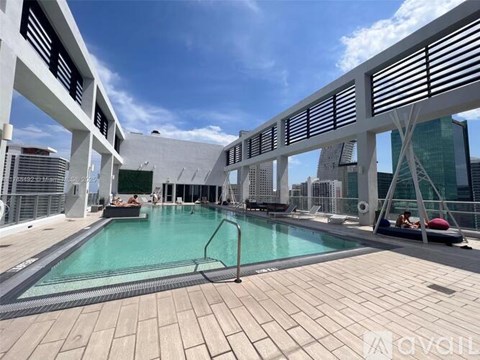 A large outdoor pool area with a sun lounger and a person sitting on it.