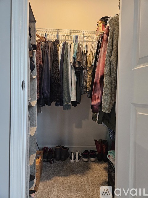 A small closet with clothes hanging and shoes on the floor.
