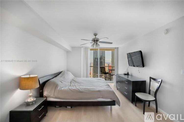 A bedroom with a bed, desk, chair, and a window overlooking a cityscape.