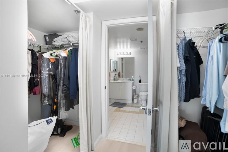 A white closet with clothes hanging and a bathroom in the background.