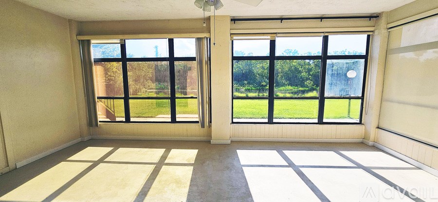 A room with a large window and a view of a green lawn and trees.