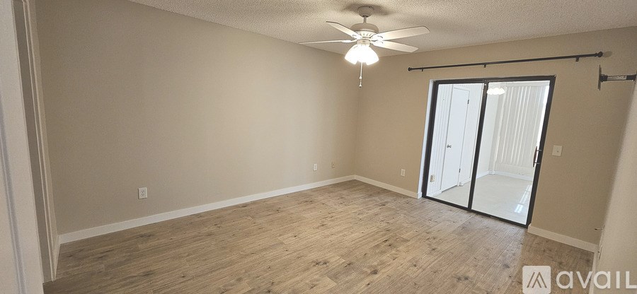 A spacious room with a ceiling fan and sliding glass doors leading to a balcony.