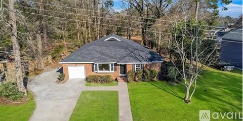 A house with a black roof and a garage is surrounded by a green lawn and trees.