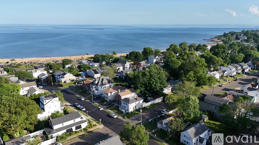 A bird's eye view of a residential area with houses, trees, and a beach in the background.