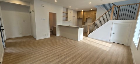 A spacious room with wooden flooring and a staircase on the right side.
