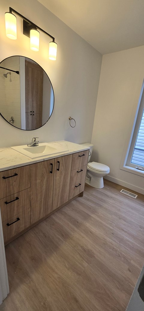 A bathroom with a round mirror, wooden cabinets, and a white toilet.