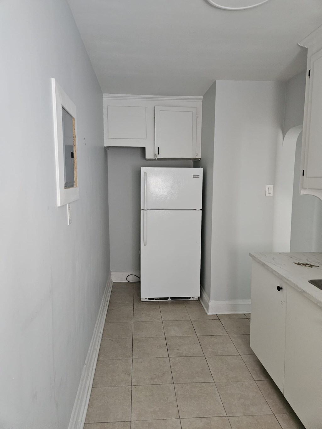 A white refrigerator in a kitchen with white cabinets.