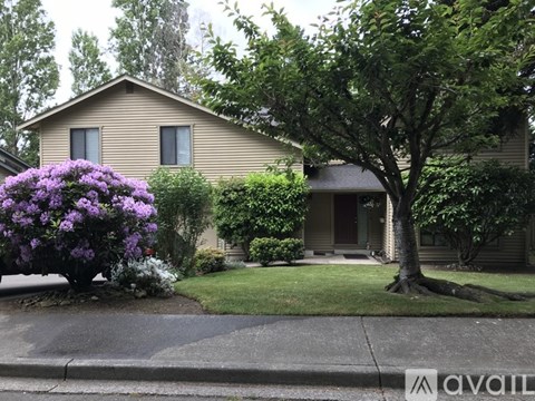 A house with a tree and a bush with purple flowers in front of it.
