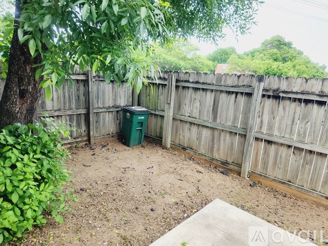 A backyard with a wooden fence and a green trash can.