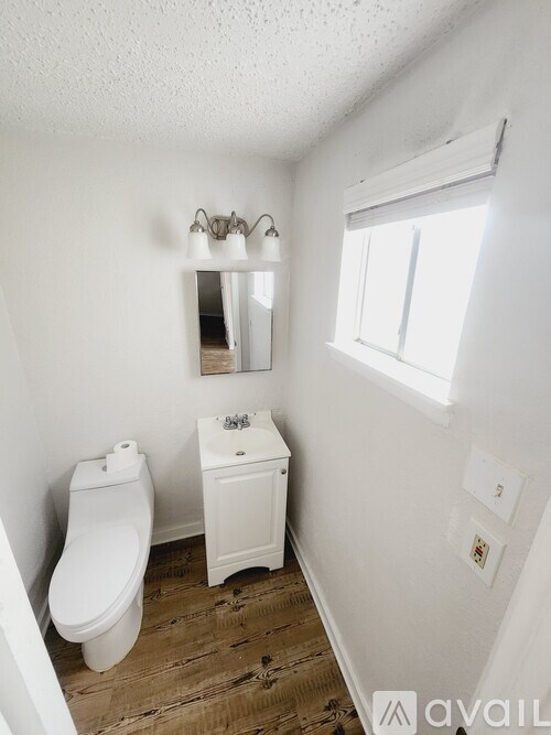 A bathroom with a toilet, sink, mirror, and wood flooring.