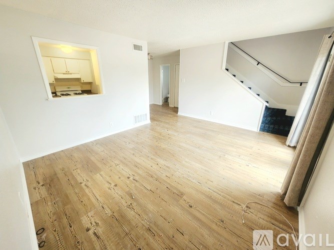 A spacious room with wooden flooring and a small kitchen area visible through a window.
