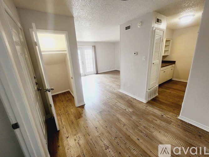 A room with wooden floors and white walls, with a kitchen area visible in the background.