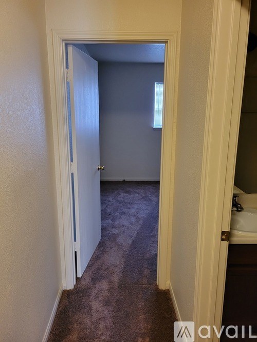 A hallway with a door on the left and a bathroom on the right.