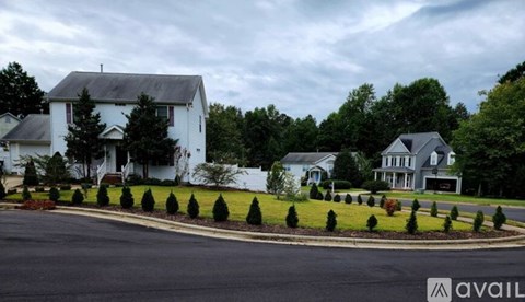 A white house with a grey roof is surrounded by green trees and bushes.