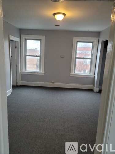 A room with grey carpet and two windows.