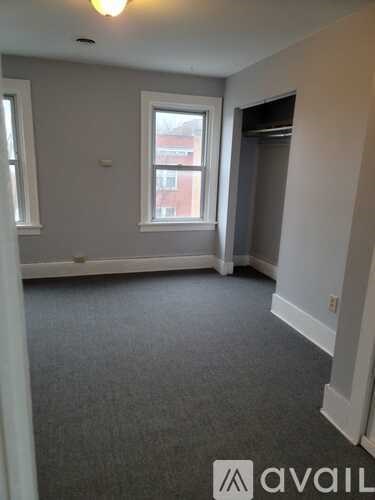 A room with grey carpet and a window overlooking a red building.