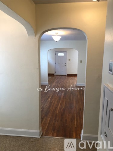 A hallway with wood flooring and white walls leading to a door.