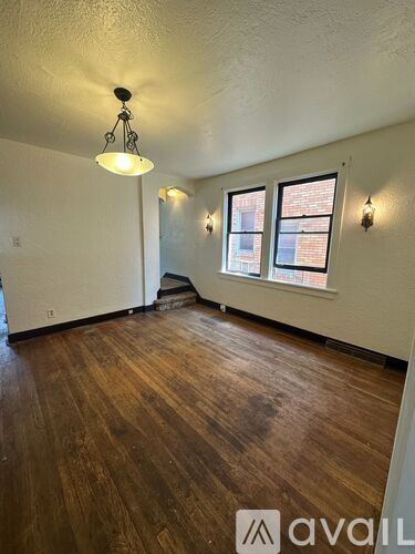 A room with wooden floors and a window with a view of a brick building.