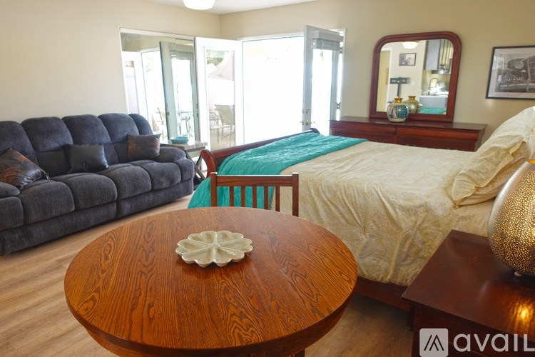 A living room with a blue couch, a wooden coffee table, and a bed with a white comforter.