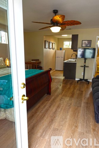 A bedroom with a bed, a dresser, a ceiling fan, and a refrigerator.