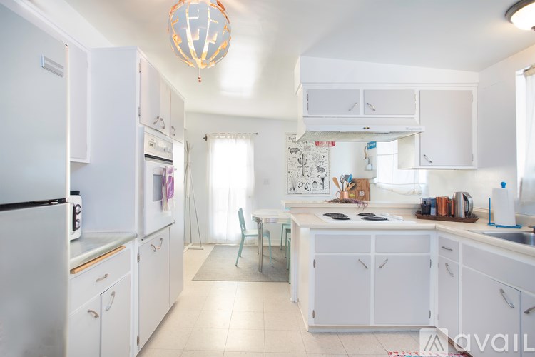 A kitchen with white cabinets and appliances, a hanging light fixture, and a window with curtains.