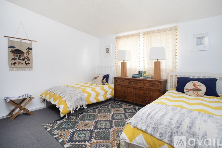 A bedroom with two beds, a bench, and a rug.