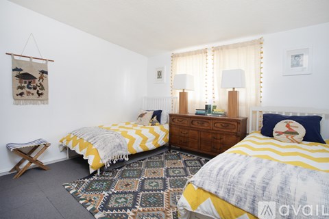 A bedroom with two beds, a bench, and a rug.