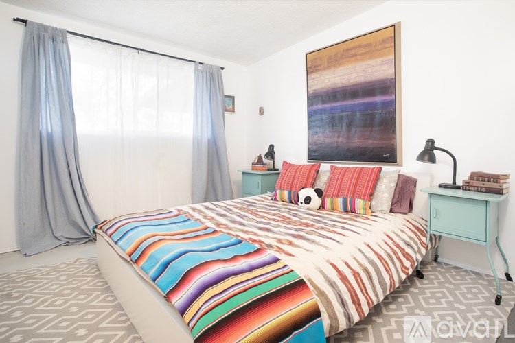 A bedroom with a colorful bedspread and a painting on the wall.