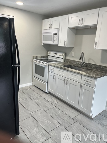 A kitchen with a black fridge, white cabinets, and a granite countertop.