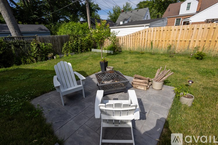 A patio with a table and chairs is surrounded by a grassy area and a wooden fence.