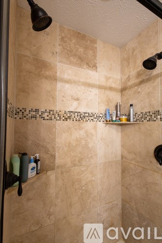 A shower with a tiled wall and a shelf with bottles on it.