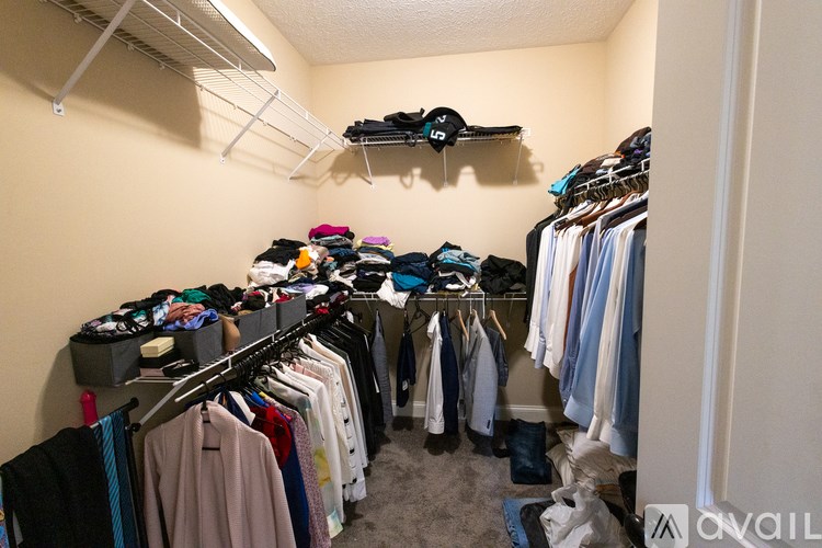 A small, messy closet with clothes on shelves and hanging on racks.