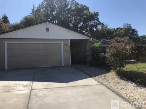 A white garage with a closed white door is surrounded by a gravel area and a small garden with pink flowers.