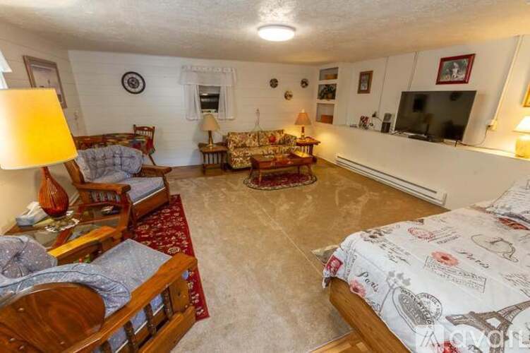 A living room with a couch, a chair, a lamp, a television, and a bed with a white comforter.