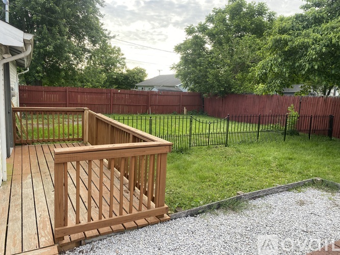 A wooden deck with a gravel area in front of a red fence.