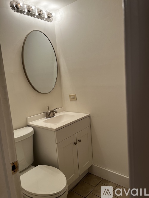 A bathroom with a toilet, sink, mirror and lights on the wall.