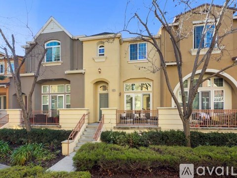 A beige two-story house with a front porch and a tree in front.